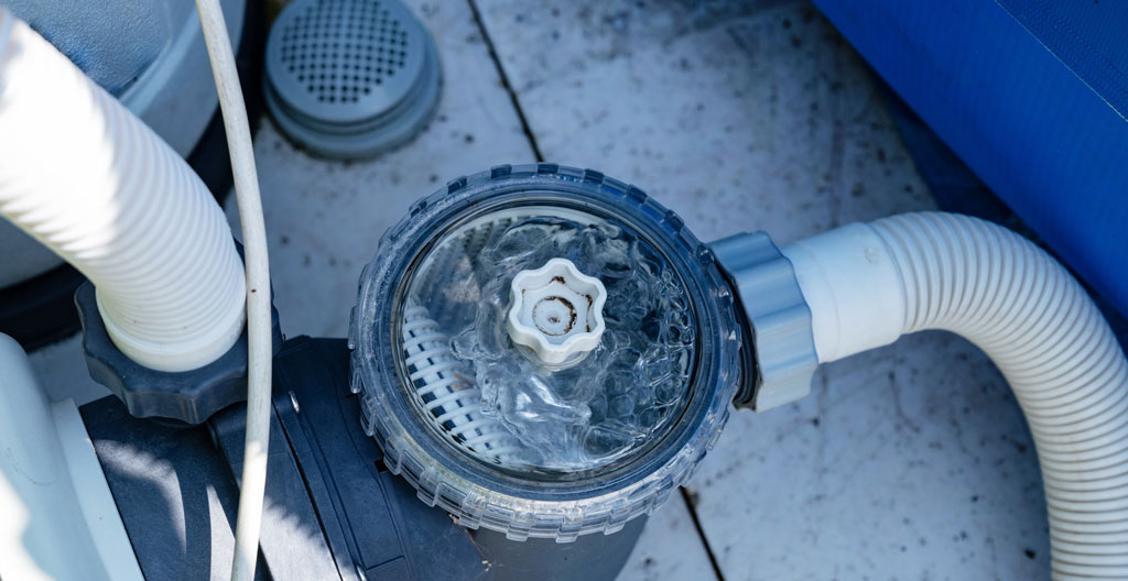 Gros plan macro sur trois textures de médias filtrants posés sur une surface blanche : granules de sable beige à gauche, fragments de verre vert translucide au centre, nervures blanches d'une cartouche plissée à droite